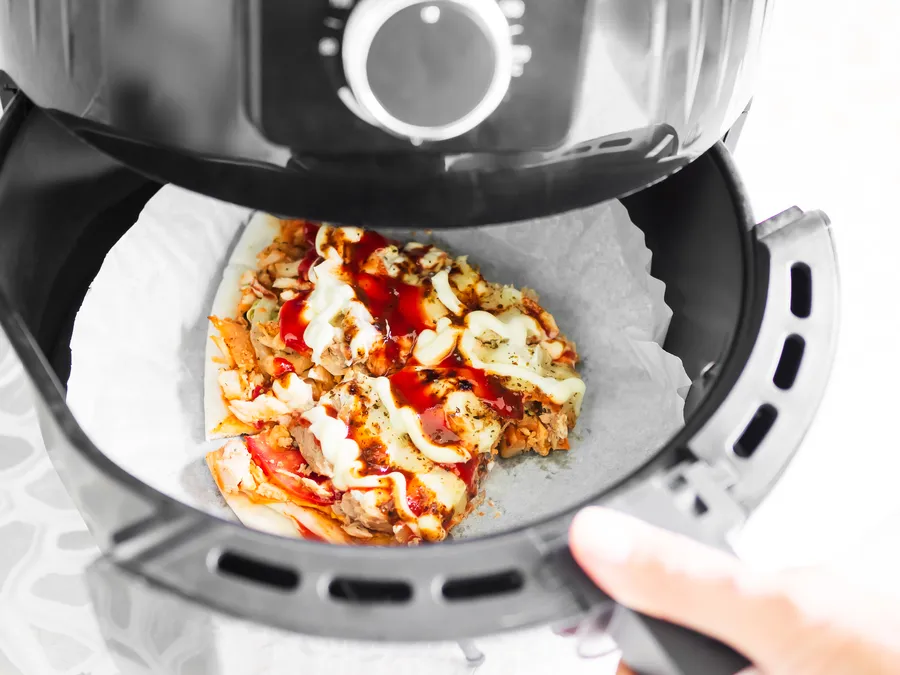 Pizza airfryerissa, päällä kastiketta ja täytteitä, valmiina tarjoiltavaksi.