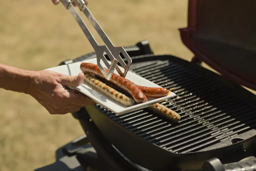 Makkaroita siirretään lautaselta sähkögrillille. Taustalla avara tilava ulkoilualue ja grillin musta ritilä.