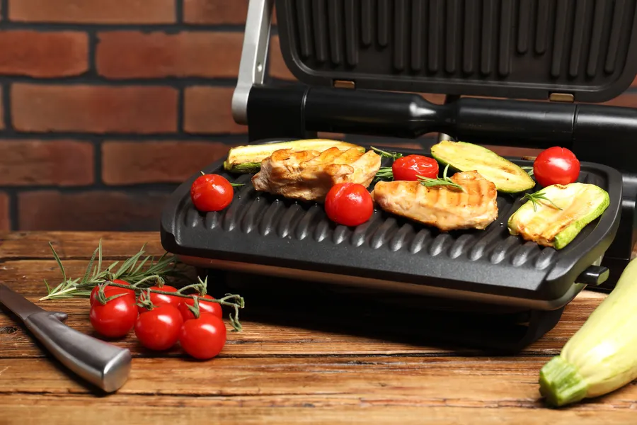 Sähkögrilli, jossa grillattuja tomaatteja ja kesäkurpitsaa, luoden maukkaan aterian.